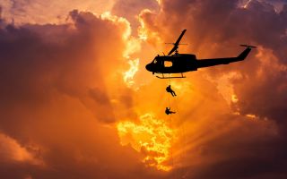 с вертолета спускаются люди по канату на фоне зарева в небе